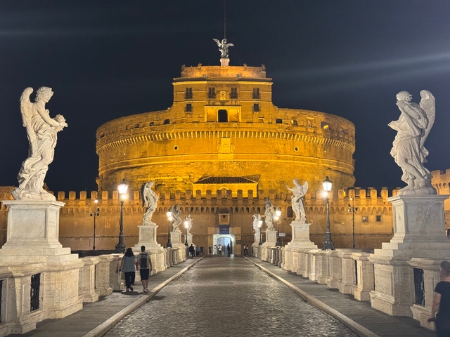Angel statues line the bridge leading to the illuminated Castel Sant'Angelo in Rome at night.