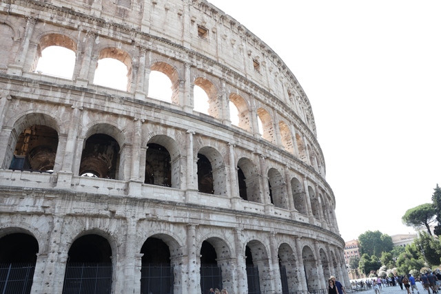Close-up view of the curved, arched exterior of the Roman Colosseum with tourists walking below