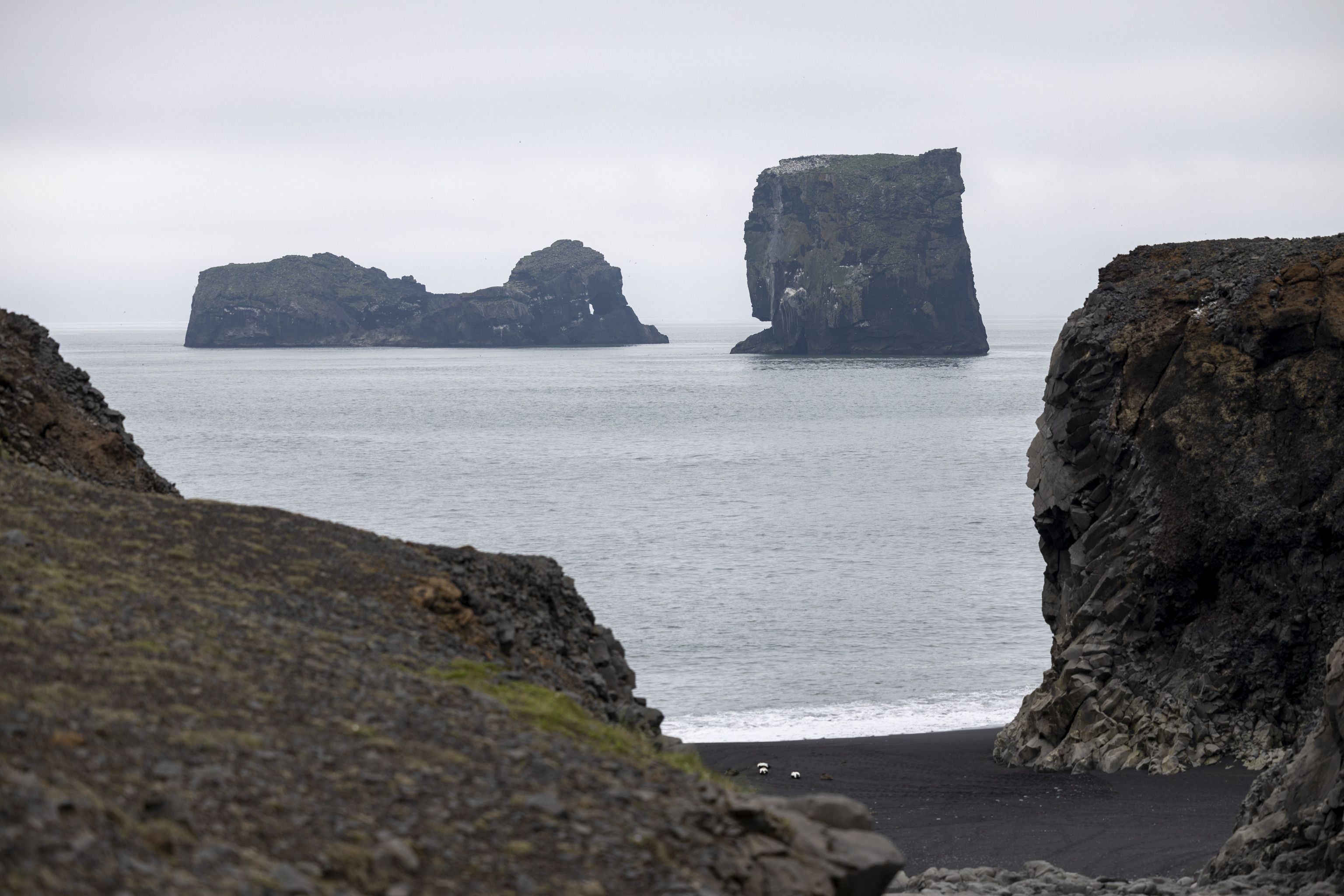 Dark volcanic sea stacks rising from the ocean beside a black sand beach in Iceland